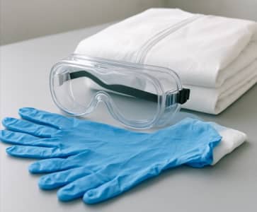 A collection of personal protective equipment including nitrile gloves, safety goggles, and a protective paint suit