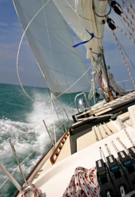 Lines and hardware on a sailboat deck being actively managed during dynamic action at sea.