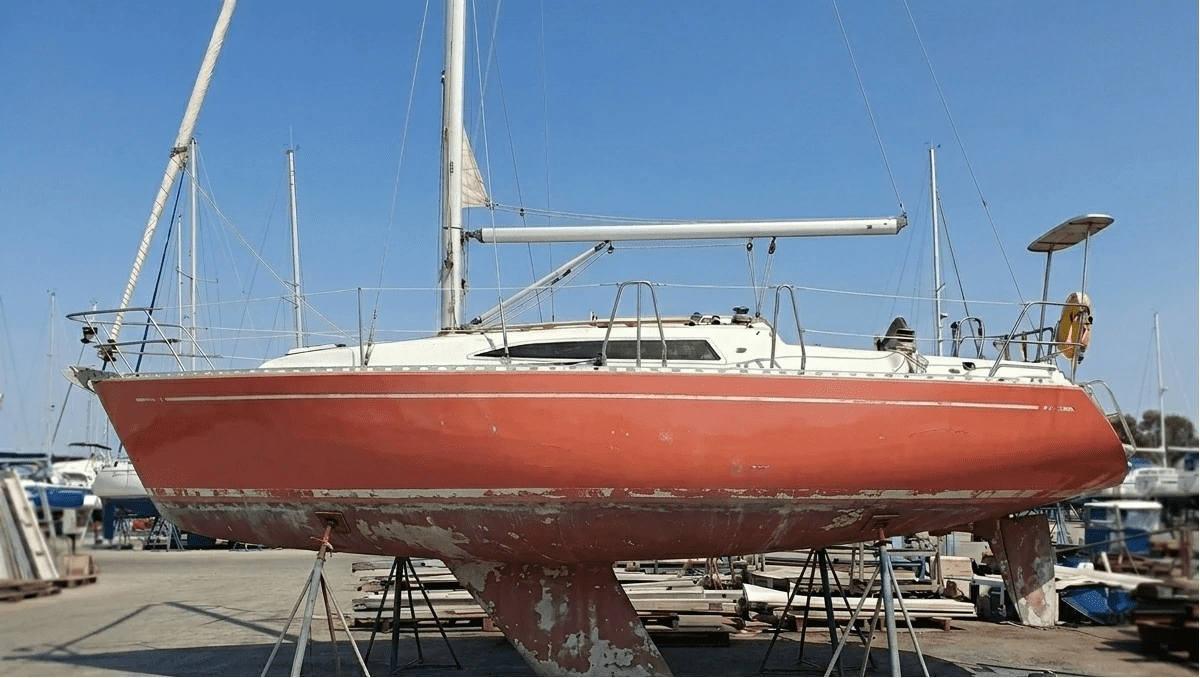 A sailboat hull exhibiting severe chalking and faded gelcoat due to UV damage and oxidation.