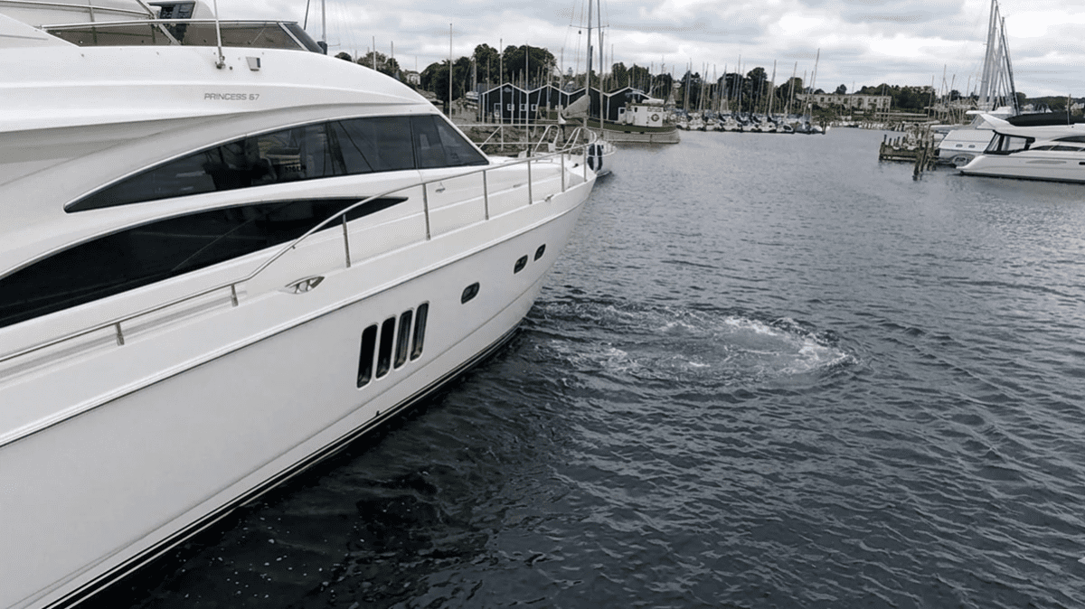 A large powerboat using a bow thruster to create lateral thrust for a precise docking maneuver in a Pacific Northwest marina.