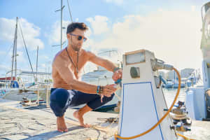 A boater connecting a heavy-duty marine shore power cord to a boat's electrical inlet for dockside battery charging.