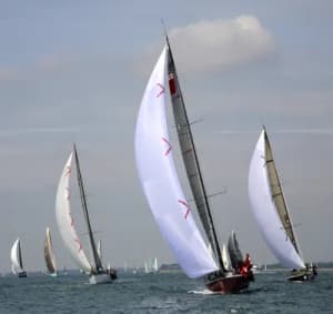 A fleet of competitive performance racing sailboats angling tightly on a racecourse under full sail.