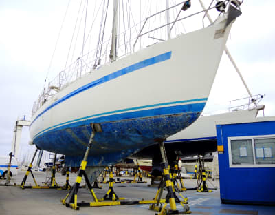 A sailboat hauled out on a shipyard hardstand undergoing hull preparation and bottom paint application.