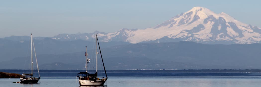 A recreational boat peacefully anchored in the Pacific Northwest with a view of Mount Rainier, demonstrating sustainable marine battery sizing storage